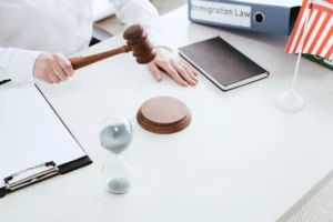 Person holding a gavel over a desk with an hourglass, U.S. flag, and ‘Immigration Law’ binder, symbolizing legal action against immigration fraud.